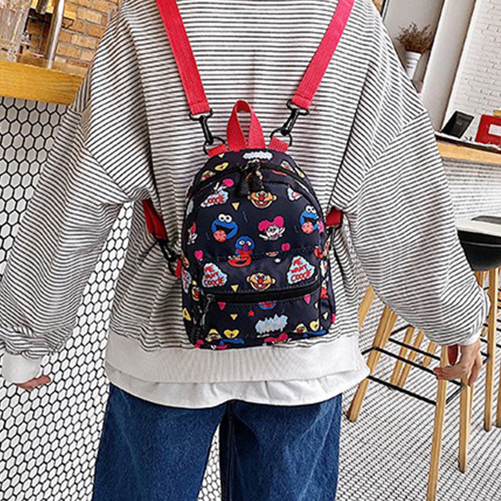 small black patterned Dollcini children’s backpack with red straps on model